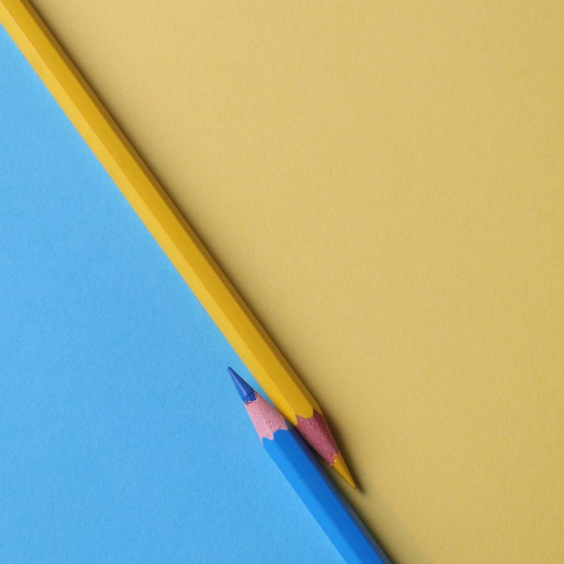 Close-up of vibrant yellow and blue colored pencils on contrasting paper backgrounds.